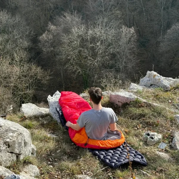matelas gonflable et sac de couchage Personne installé confortablement dans sont duvet assis sur sont matelas gonflable au bord d'une montagne.