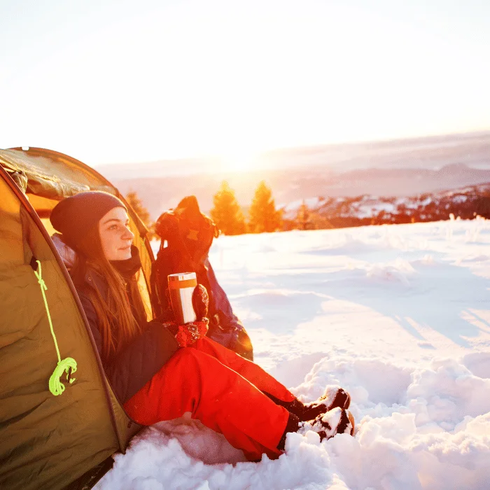 Jeune femme profitant d'un bivouac hivernal au lever du soleil, idée parfaite de cadeau bivouac Noël pour les amateurs d'aventure en plein air.