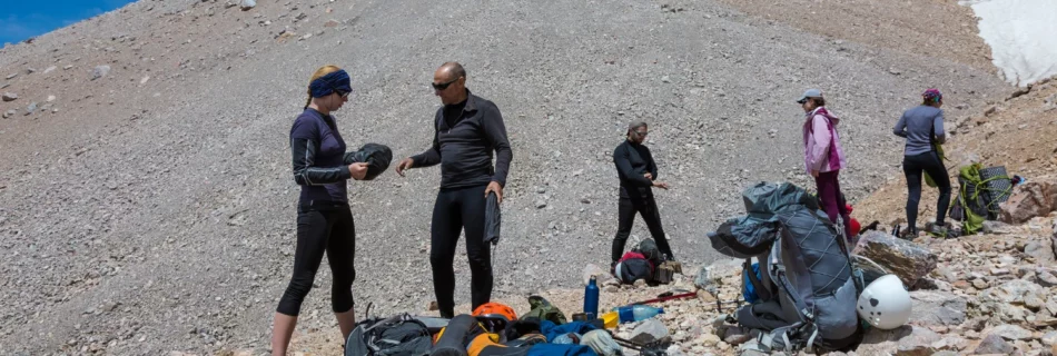 Un groupe de randonneurs prépare leur équipement de bivouac en montagne, organisant sacs, casques et matériel de sécurité pour une expédition bien équipée. Idéal pour illustrer l'importance de la préparation et des bons outils en pleine nature.