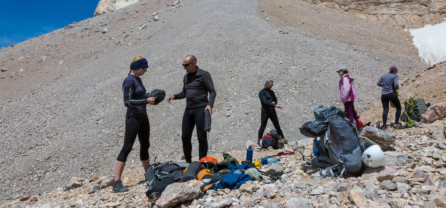 Un groupe de randonneurs prépare leur équipement de bivouac en montagne, organisant sacs, casques et matériel de sécurité pour une expédition bien équipée. Idéal pour illustrer l'importance de la préparation et des bons outils en pleine nature.