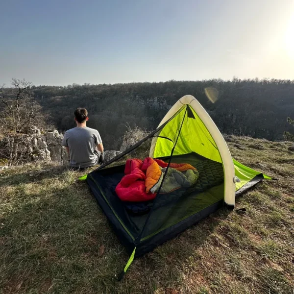 personne assis à coté de sa tente regardant l'horizon avec dedans sont duvet en boule