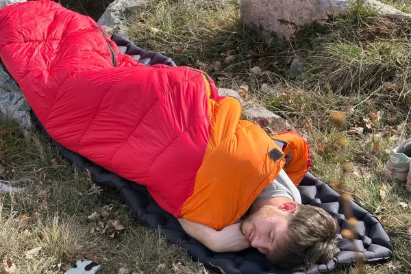 personne qui fait un dodo dans un duvet sur un matelat de bivouac lors d'un trek