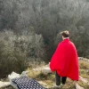 personne observant debout au bord de la montagne avec un duvet sur ses épaules et à coté un matelas gonflable de trek
