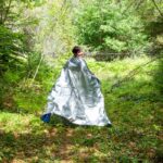 jeune femme se promenant dans la nature avec une couverture de survie sur le dos