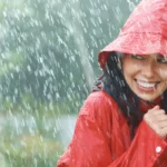 Femme souriante portant un poncho rouge sous une pluie battante en pleine nature.