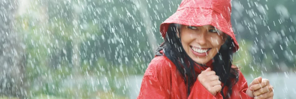 Femme souriante portant un poncho rouge sous une pluie battante en pleine nature.