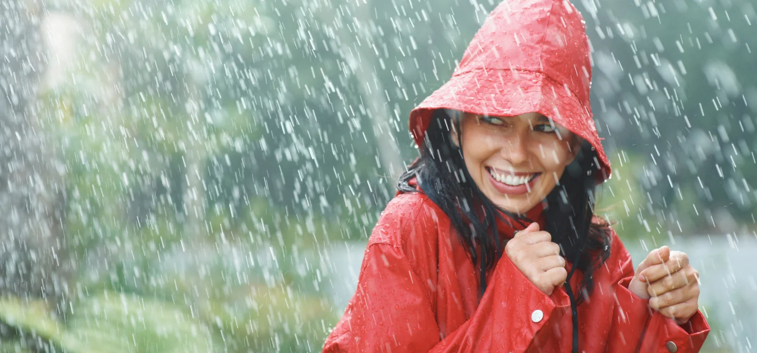 Femme souriante portant un poncho rouge sous une pluie battante en pleine nature.