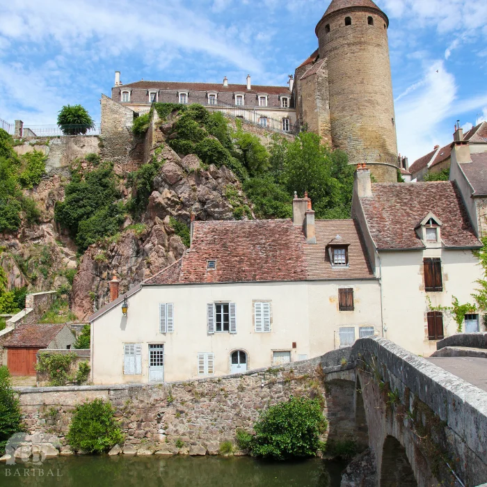 Vue sur un pont avec le passage d'une rivière en dessous et après ce pont apparait un château