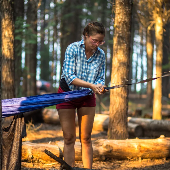 une femme qui attache sont hamac sur un arbre dans la foret