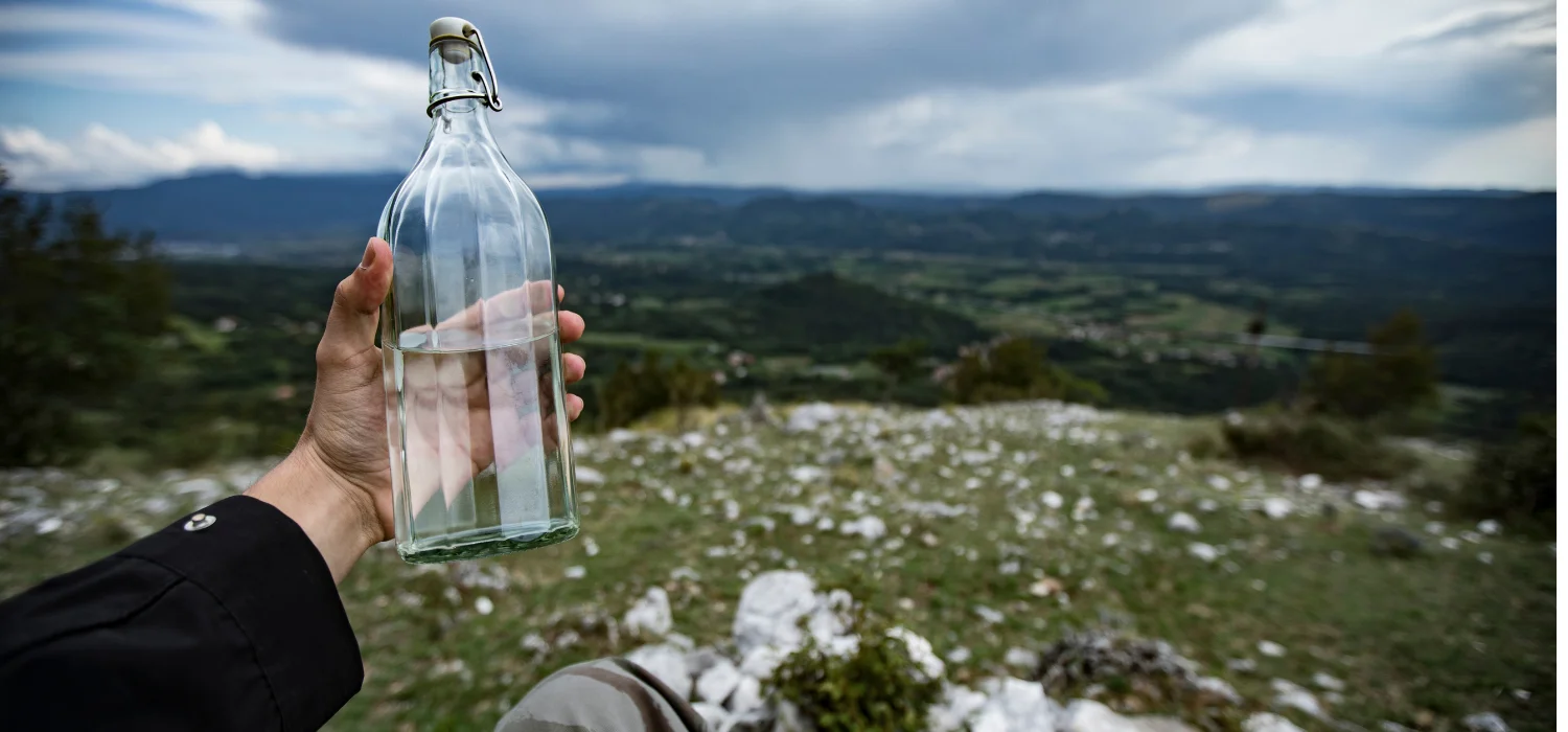 Personne sortant une bouteille d'eau en verre devant une vue magnifique