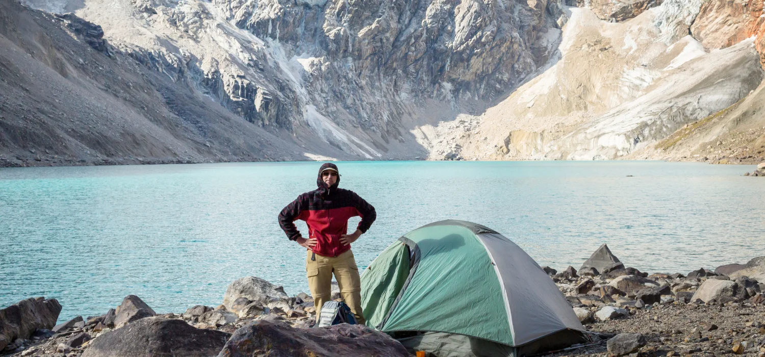 homme debout à coté de sa tente installé au bord d'un super lac dans les montagnes