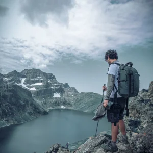 un homme au bord d'un lac en montagne avec un sac de rando