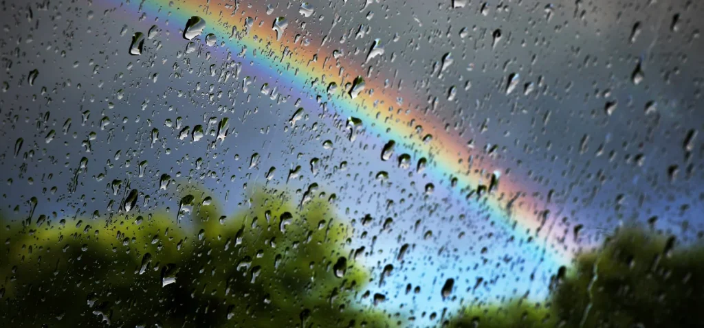 pluie sur un carreau avec dans le fond un grand arc en ciel